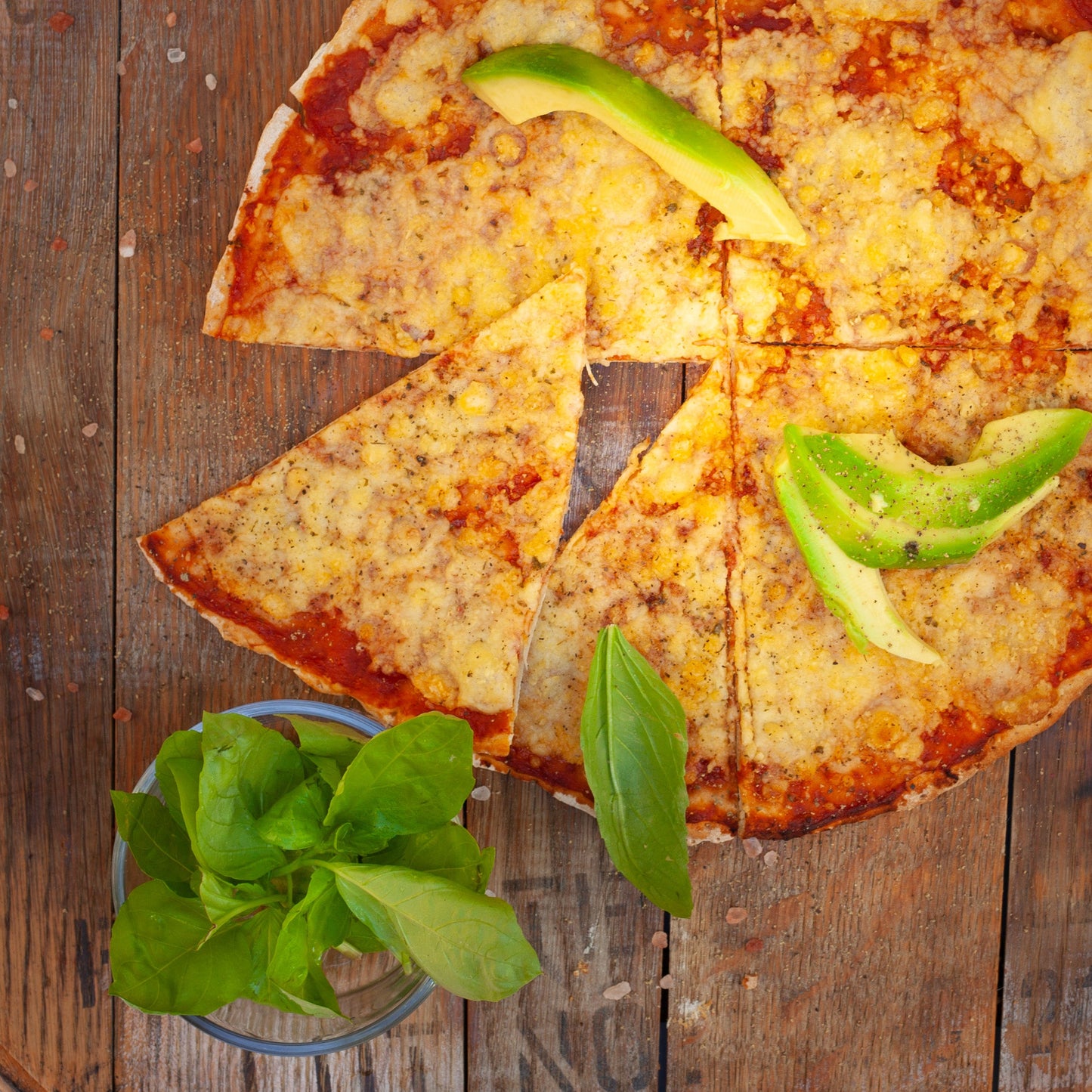 Cheesy vegan margherita pizza with avocado slices on a wooden surface