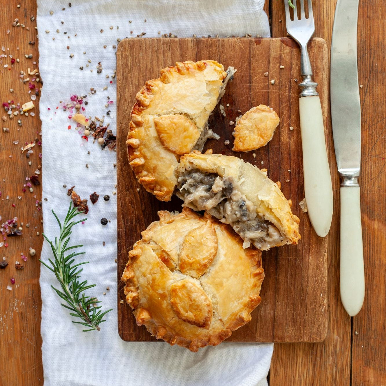 Two vegan chicken mushroom pies on a wooden cutting board on a rustic wooden table.