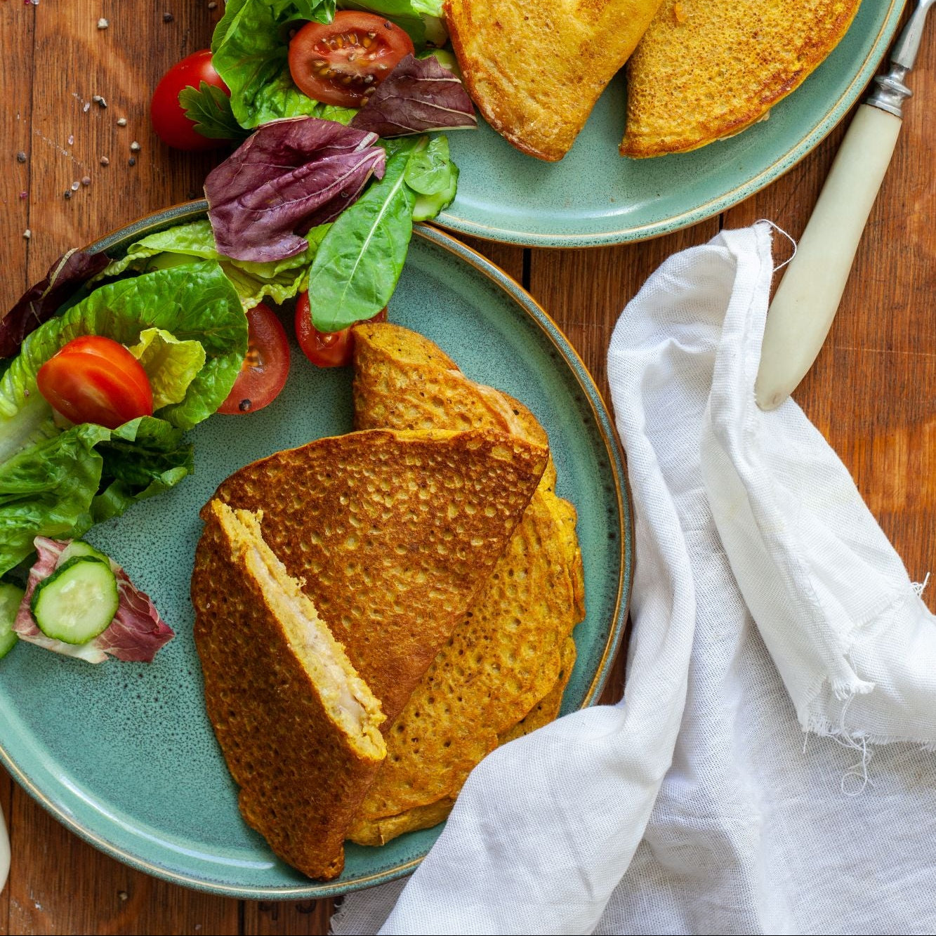 Two plates of food with vegan mung bean omelette, vegetables and greens on a wooden table