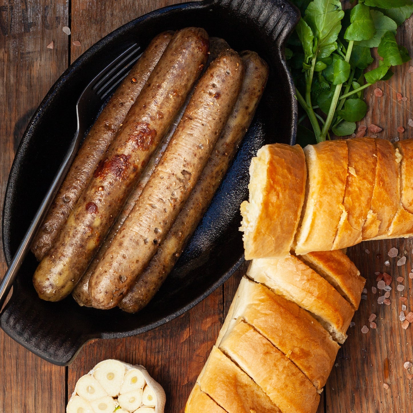 Vegan boerewors plant-based sausage in a black dish with bread and garlic on a wooden surface
