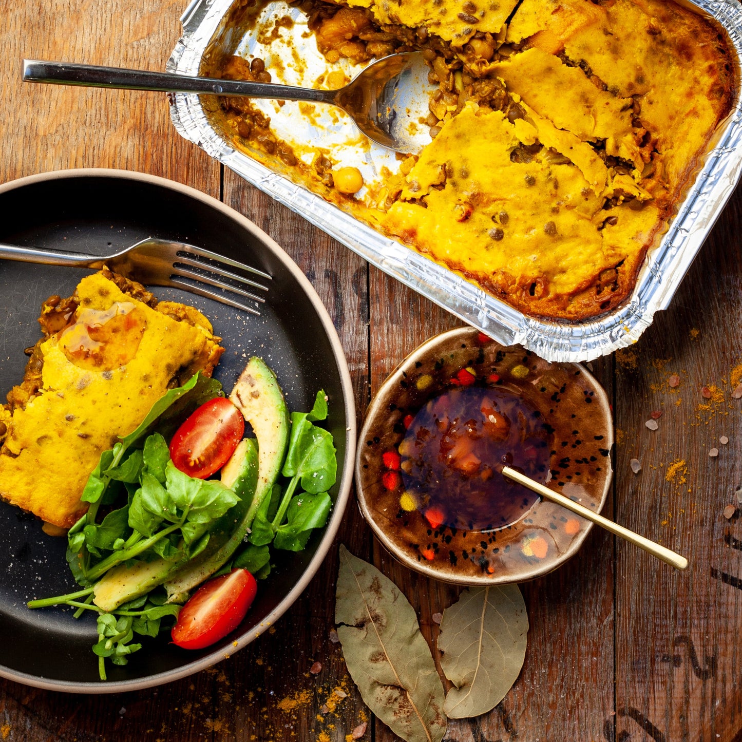 vegan bobotie on a wooden table with a side salad and sauce.