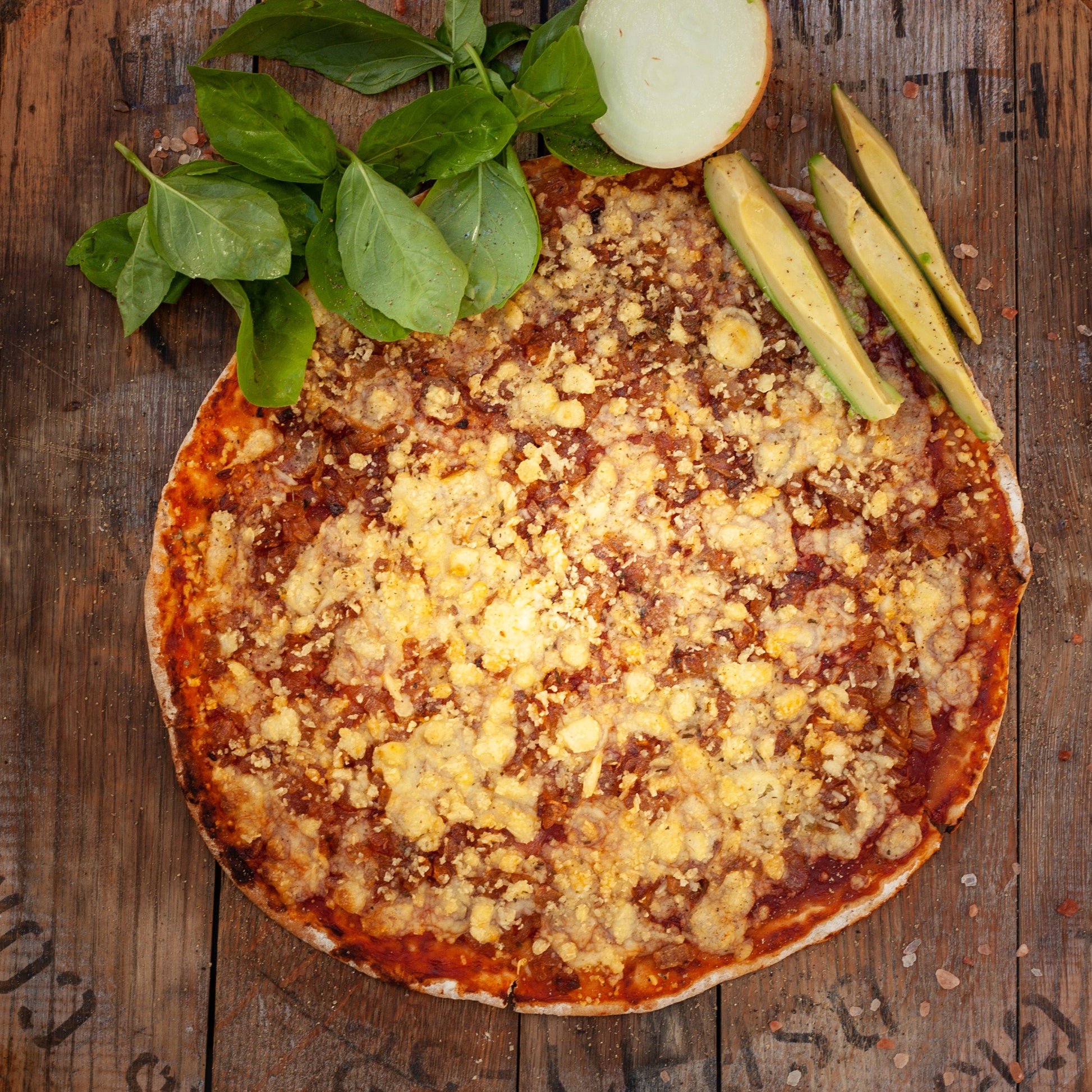 vegan caramelised onion pizza with vegan cheese, basil, and avocado served on a wooden surface