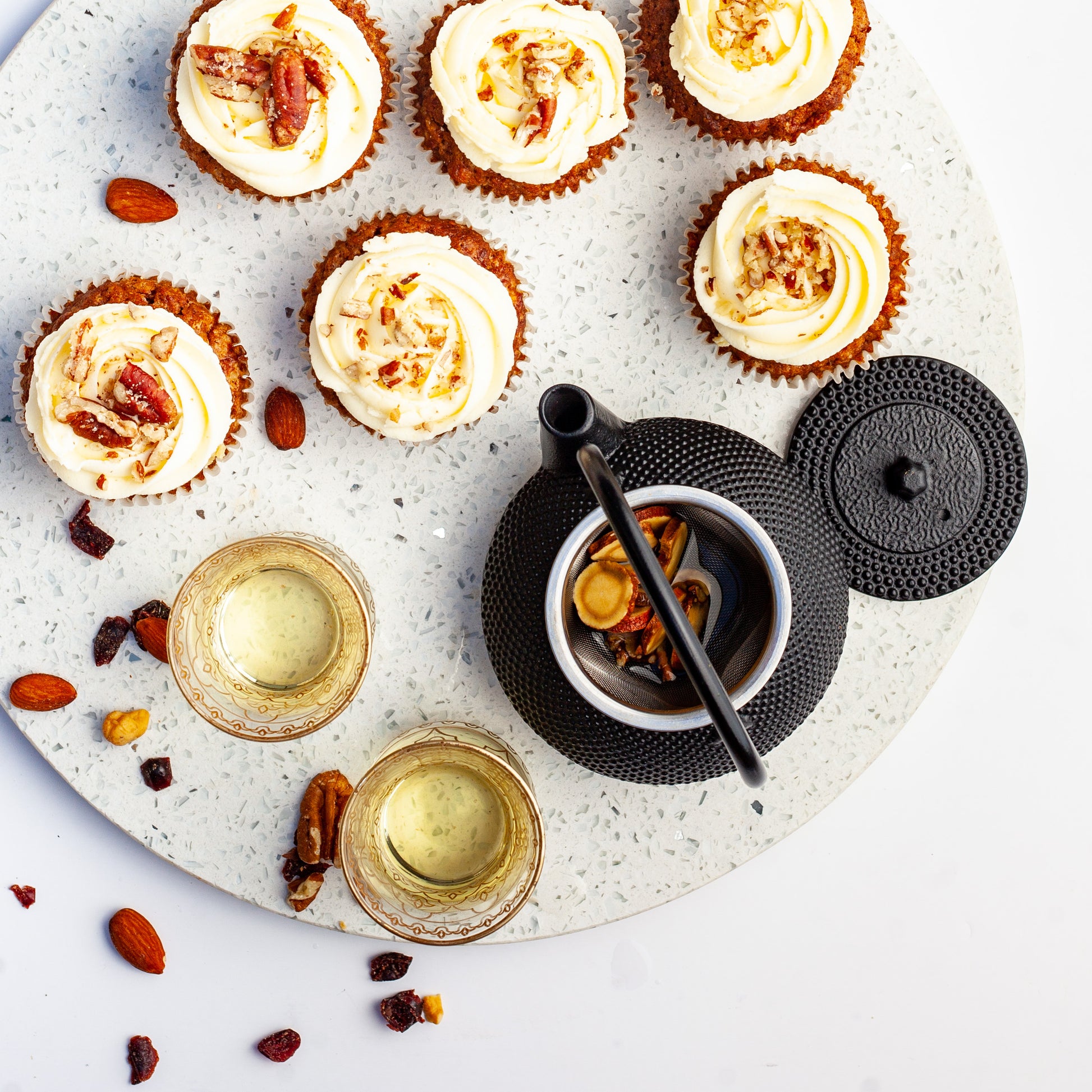 Vegan carrot cupcakes with white frosting and nuts on a round stone board with herbal tea.
