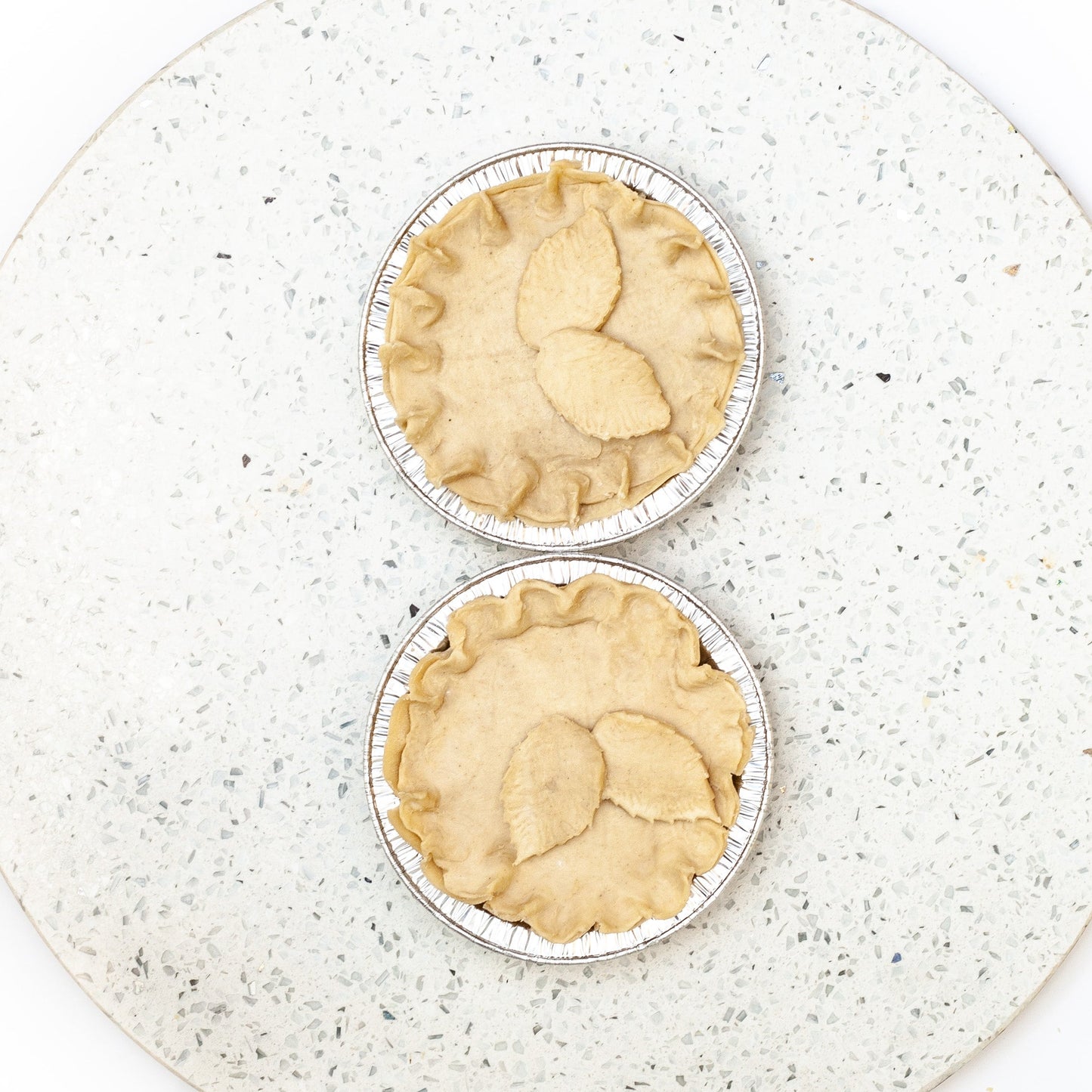 Two vegan chicken mushroom pies in metal pie tins on a speckled white plate.