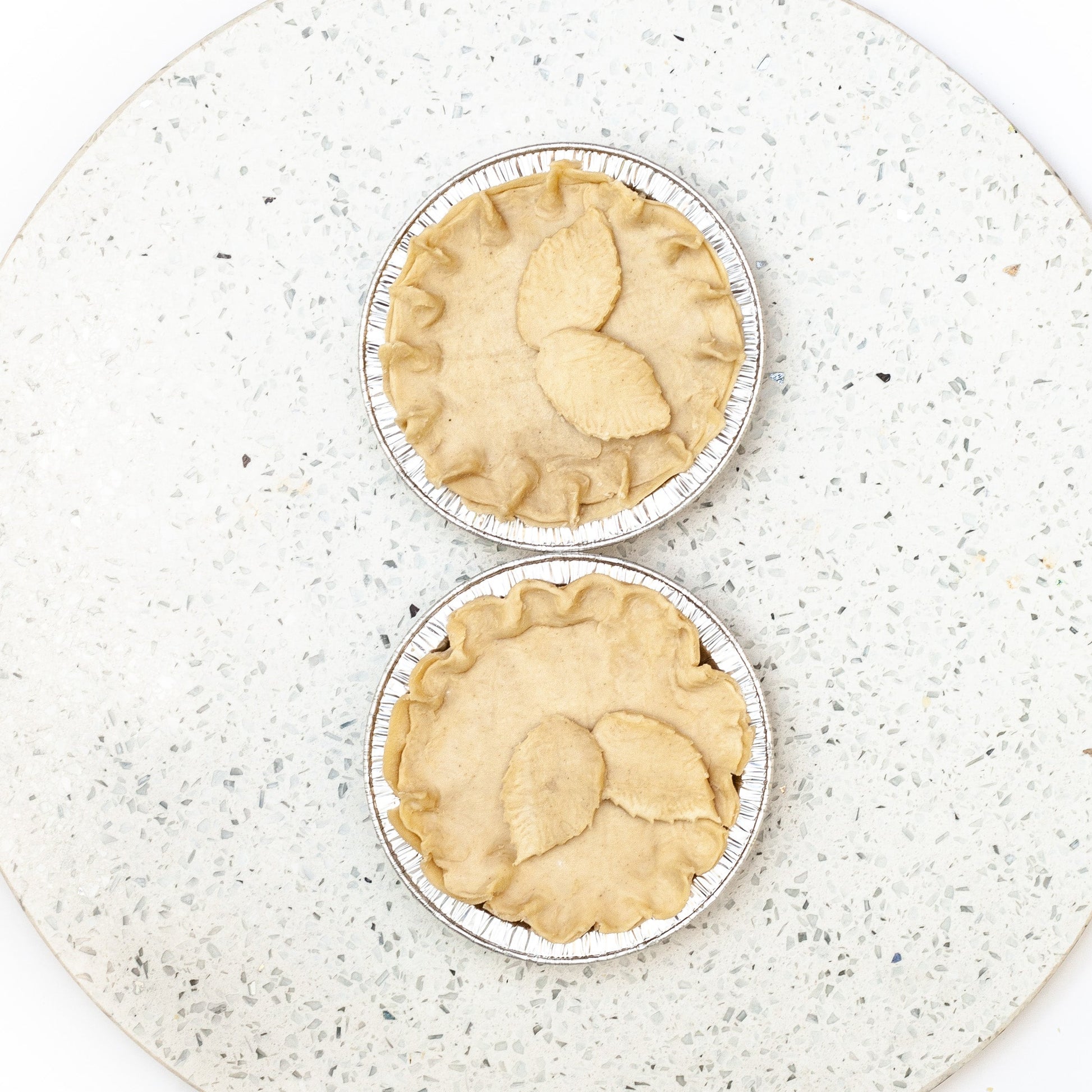 Two vegan chicken mushroom pies in metal pie tins on a speckled white plate.