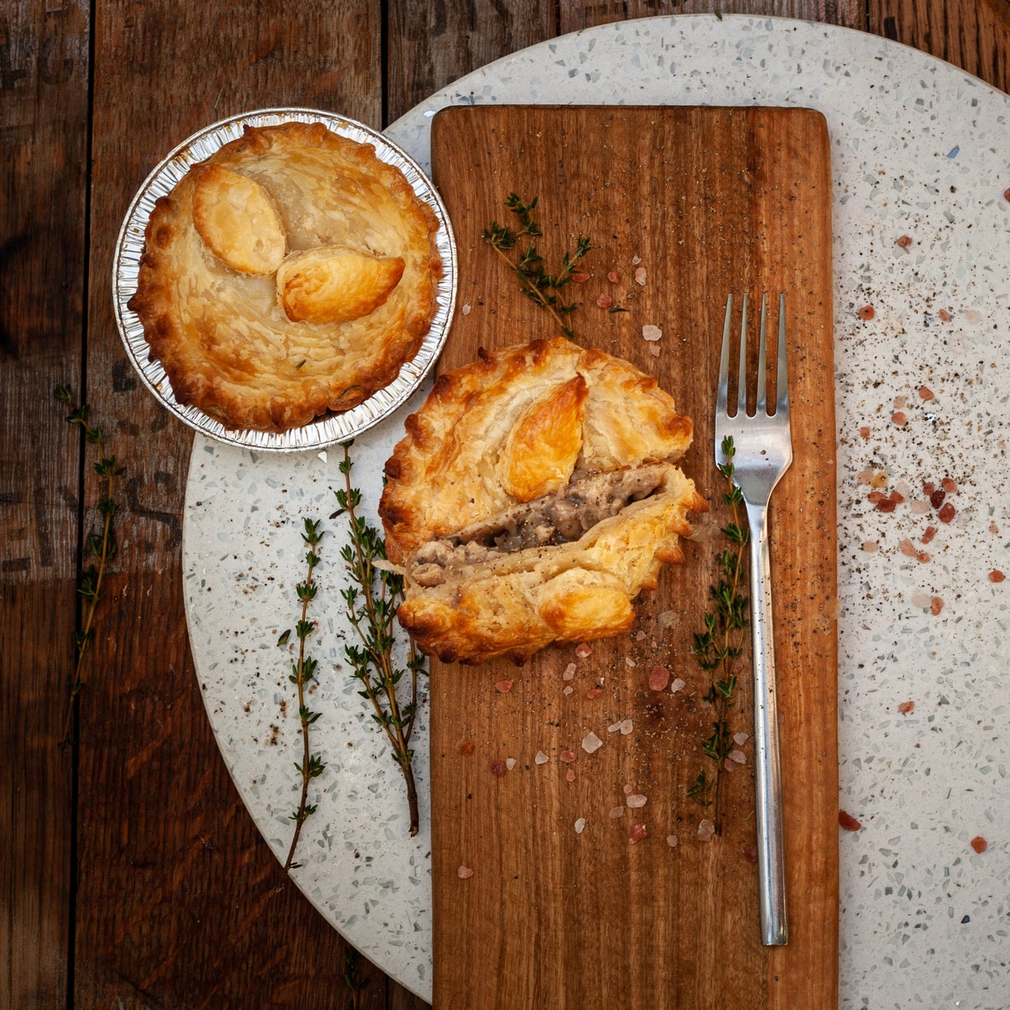 Two vegan chicken mushroom pies on a wooden cutting board with a fork, on a rustic wooden table.