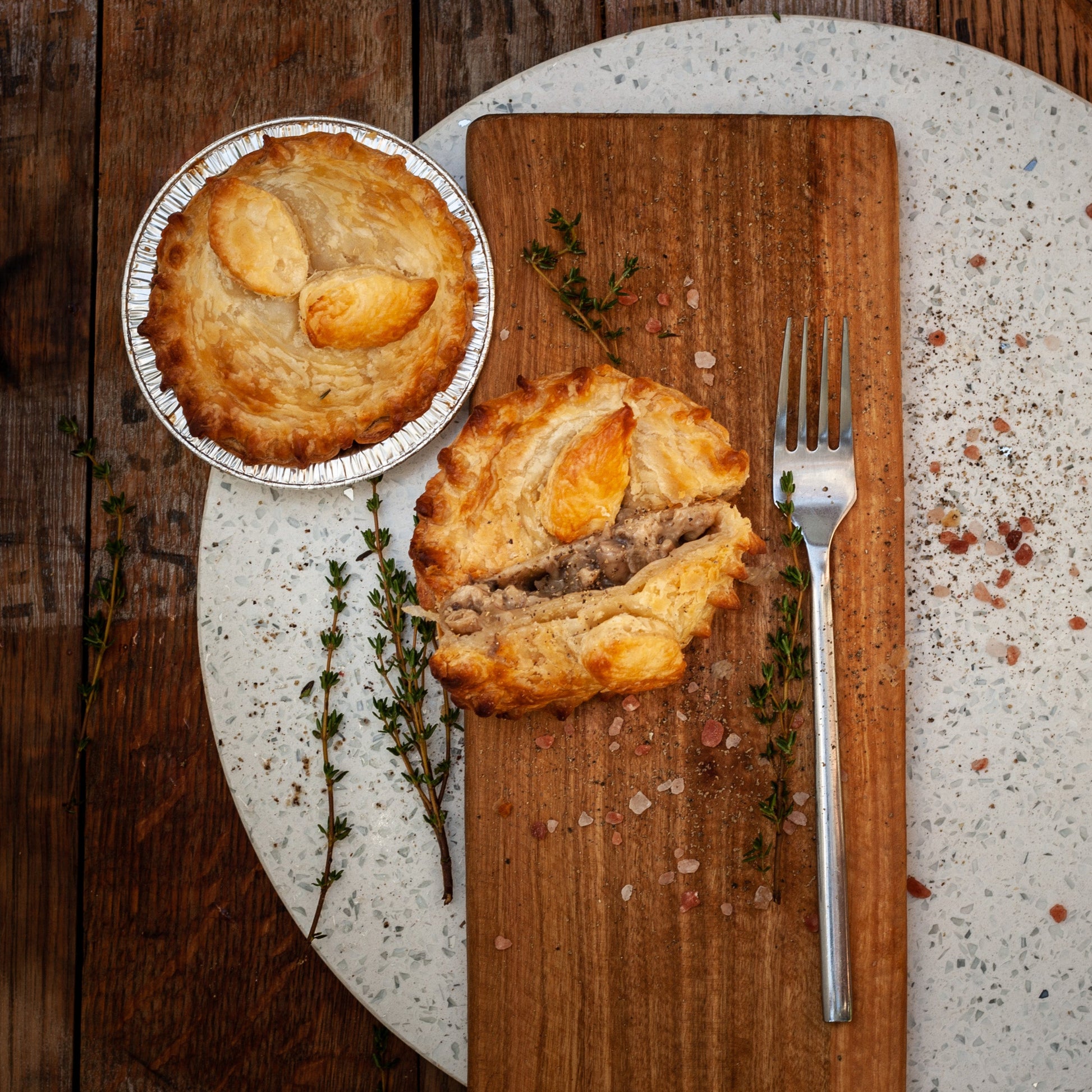 Two vegan chicken mushroom pies on a wooden cutting board with a fork, on a rustic wooden table.