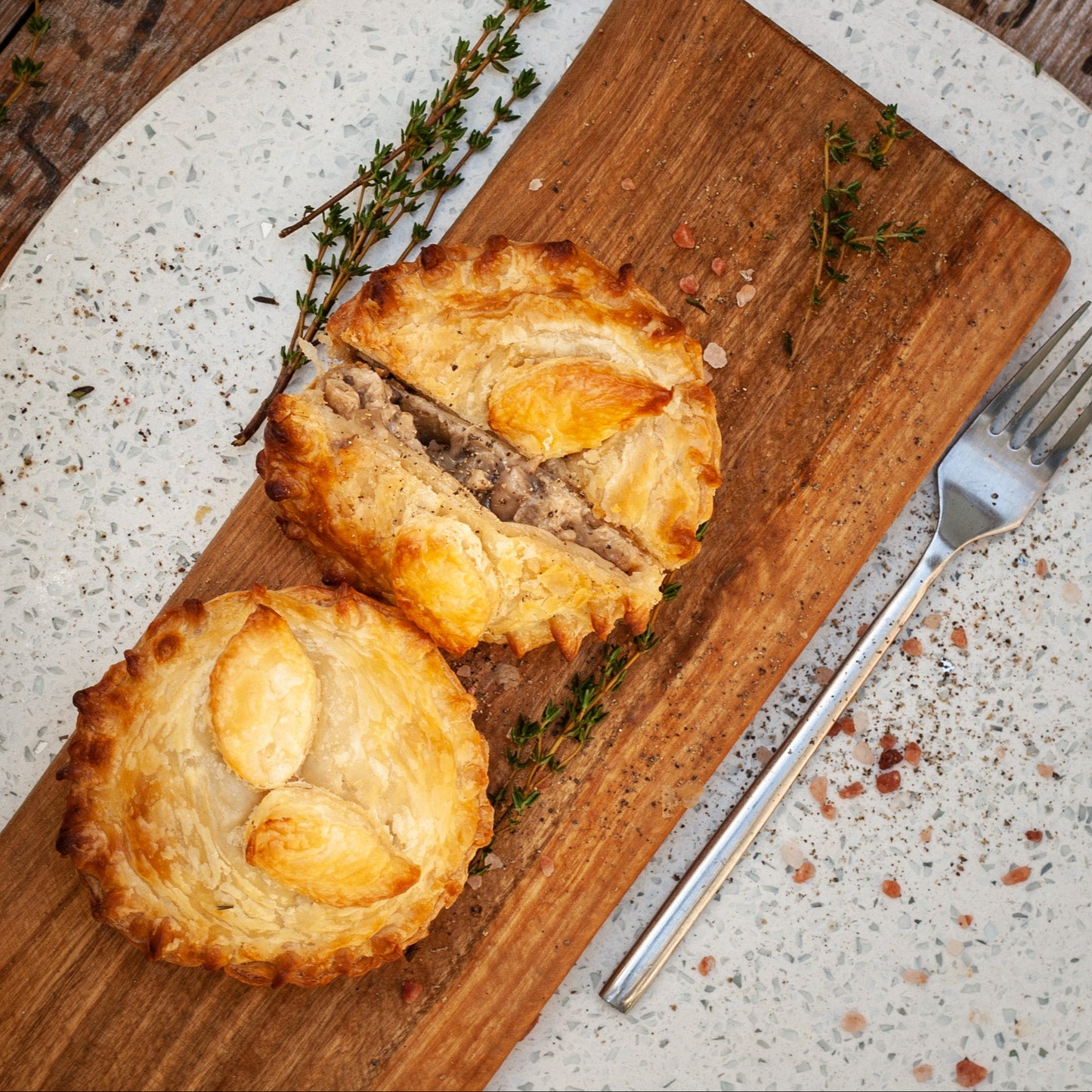 Two sliced vegan chicken mushroom pies on a wooden cutting board with thyme sprigs, on a rustic wooden surface.