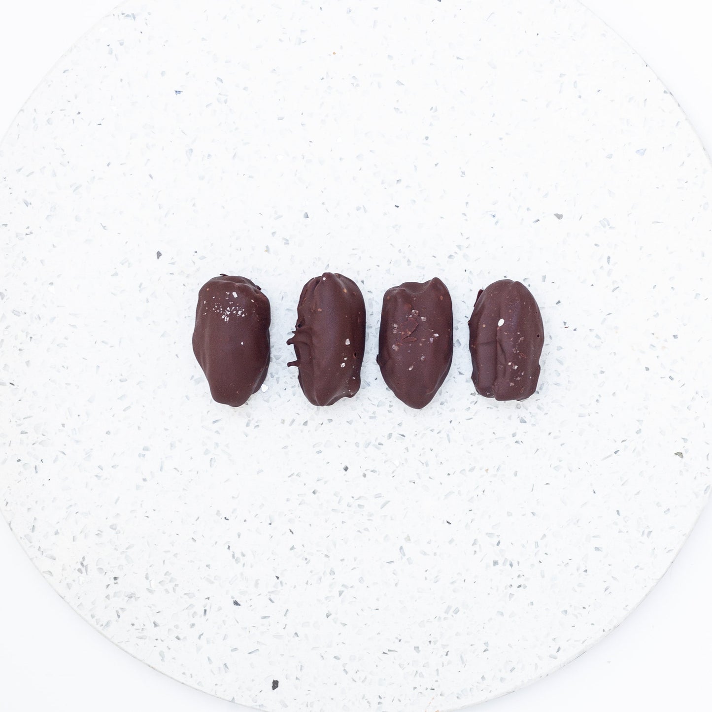 Four dark chocolate covered vegan date energy balls on a speckled white plate.