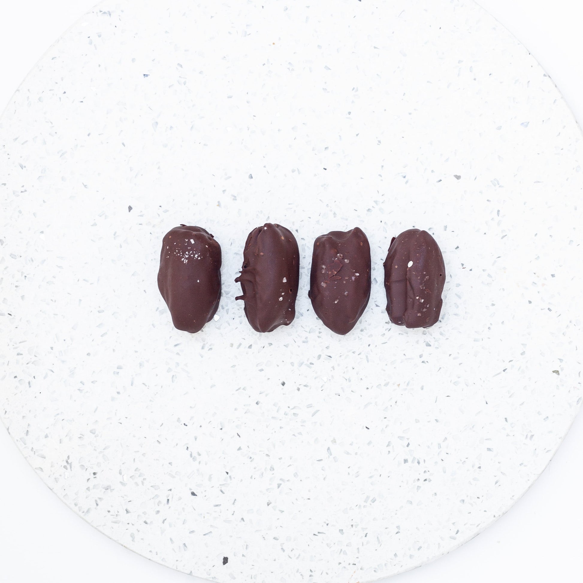 Four dark chocolate covered vegan date energy balls on a speckled white plate.
