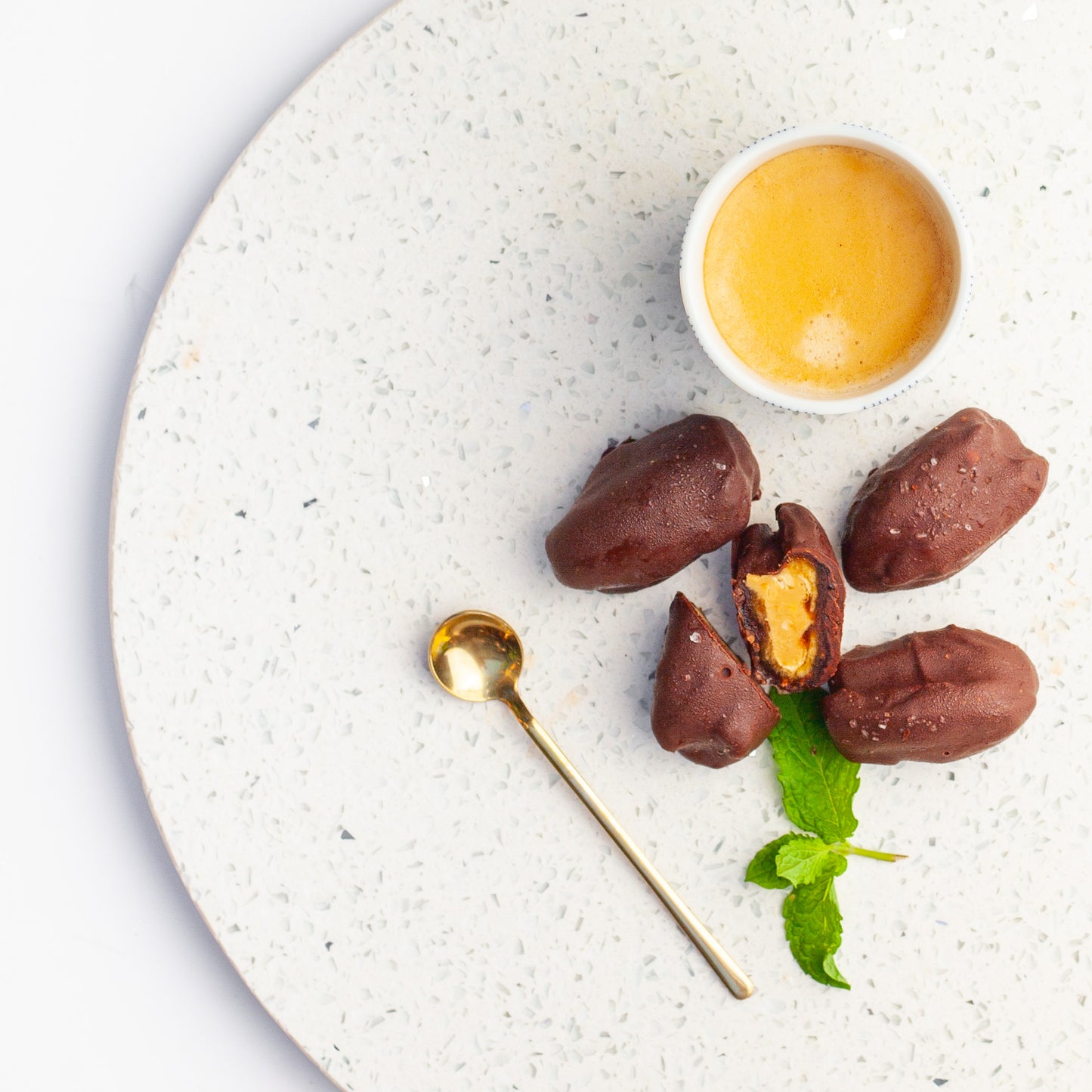 Chocolate covered vegan date energy balls with peanut butter inside, served on a speckled plate.