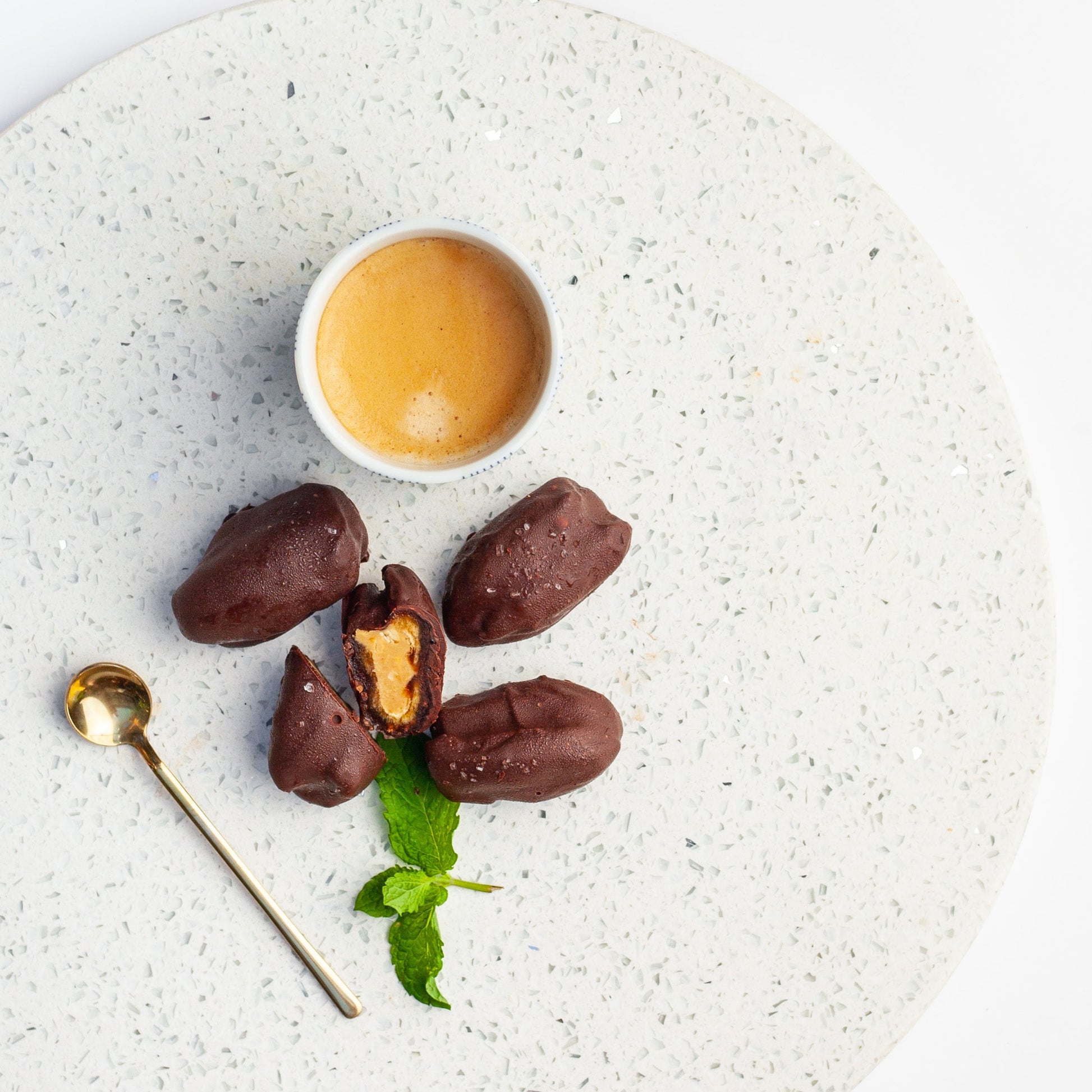 Chocolate covered vegan date energy balls with peanut butter inside, served on a speckled plate.