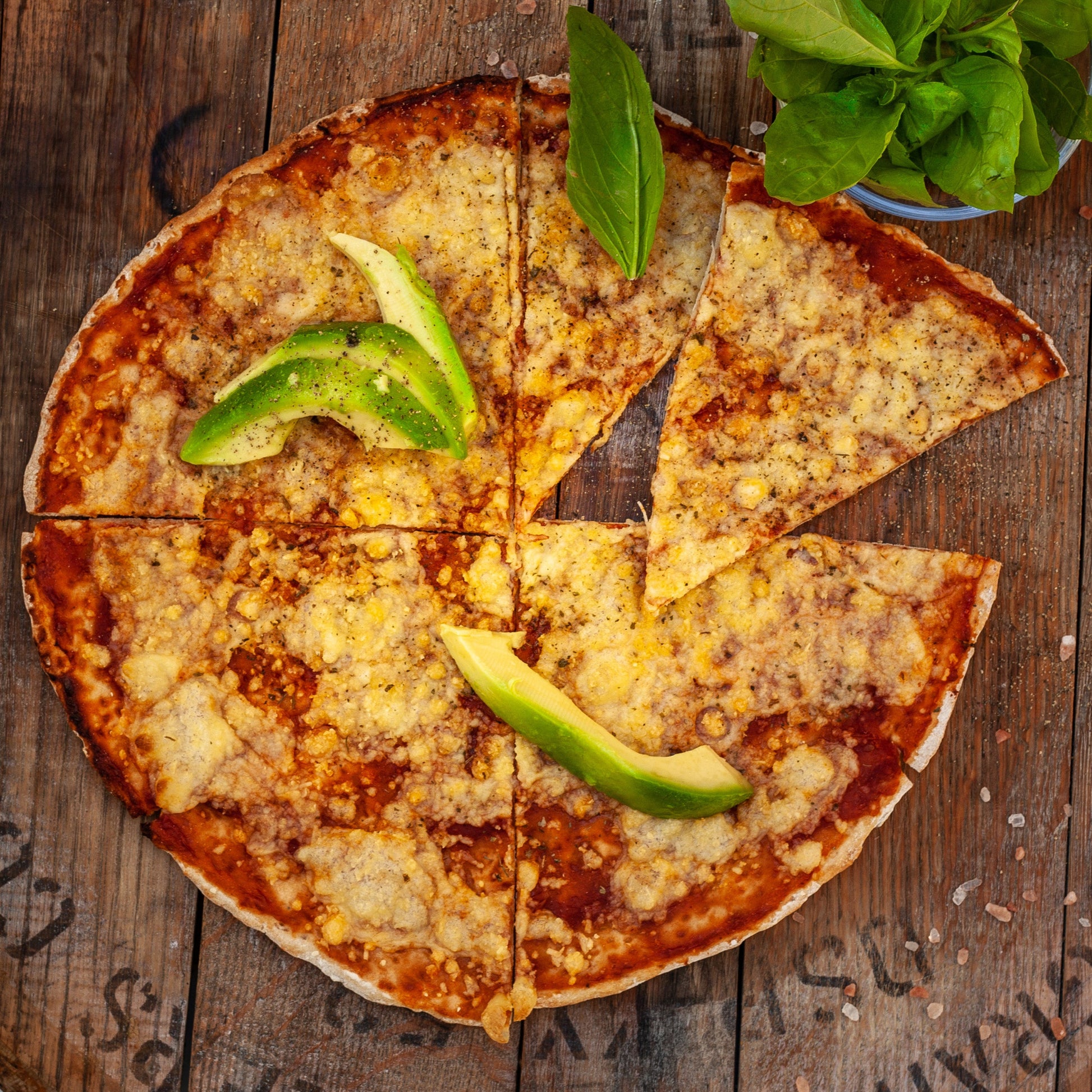 vegan margherita pizza with vegan cheese and avocado slices on a wooden surface