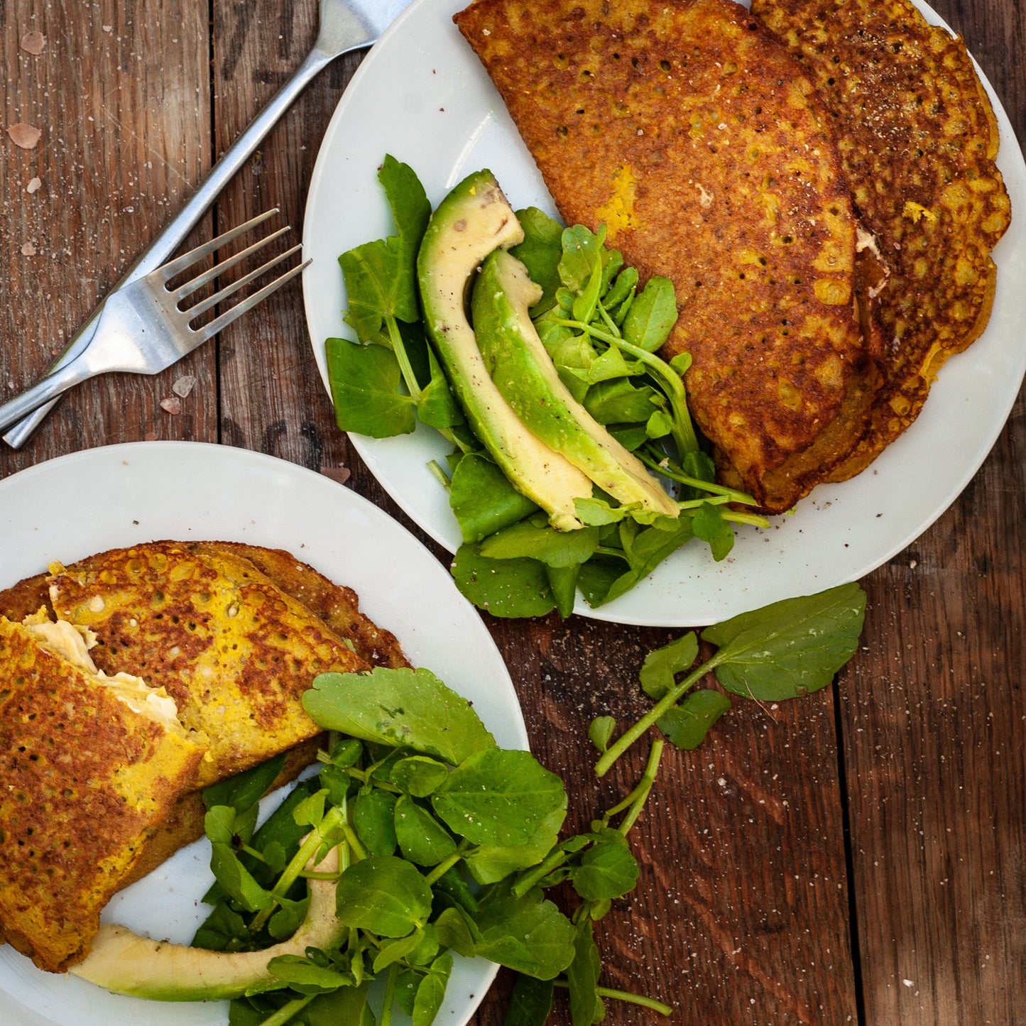 Two plates of food with vegan mung bean omelette, avocado and greens on a wooden table