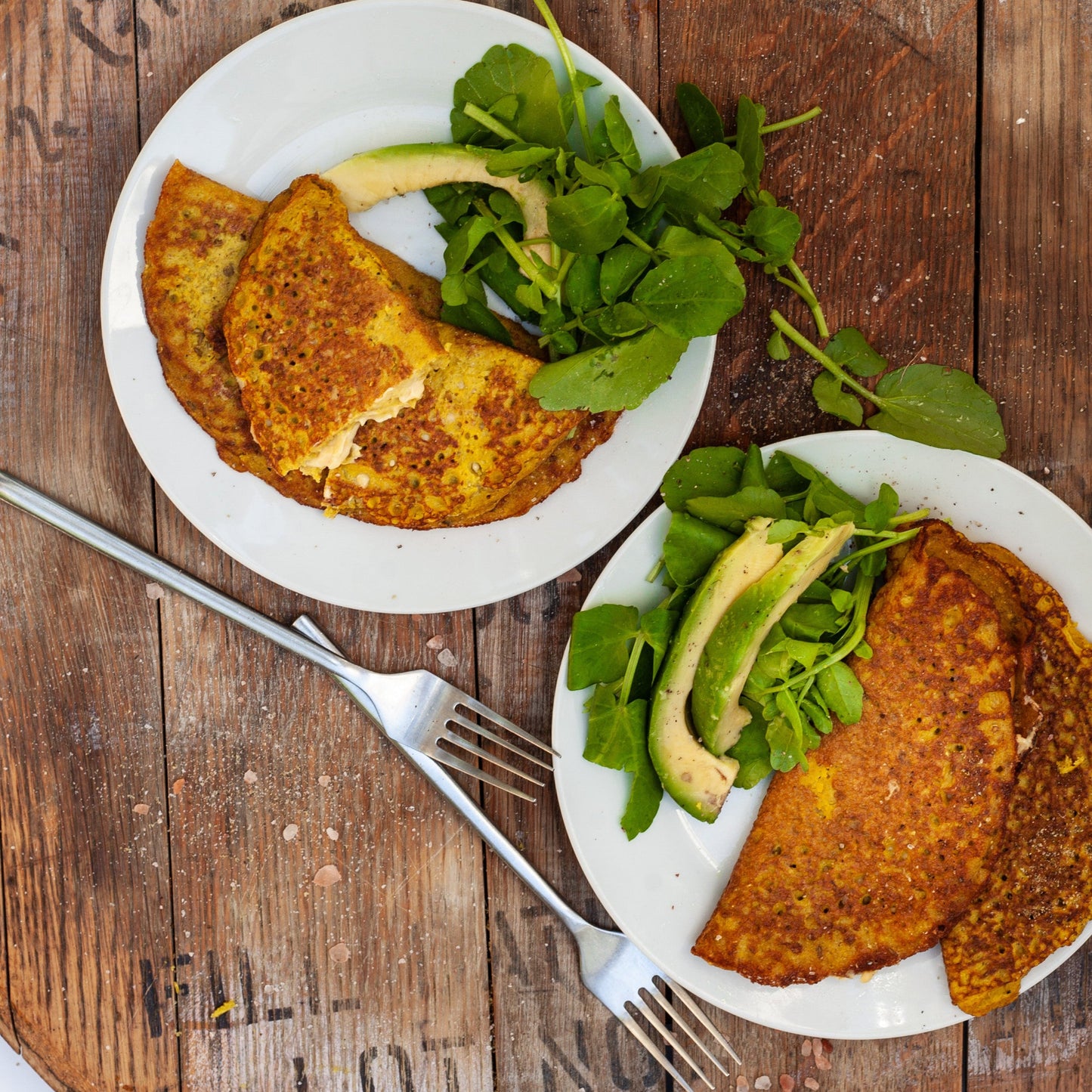 Two plates of vegan mung bean omelette with avocado and greens on a wooden table