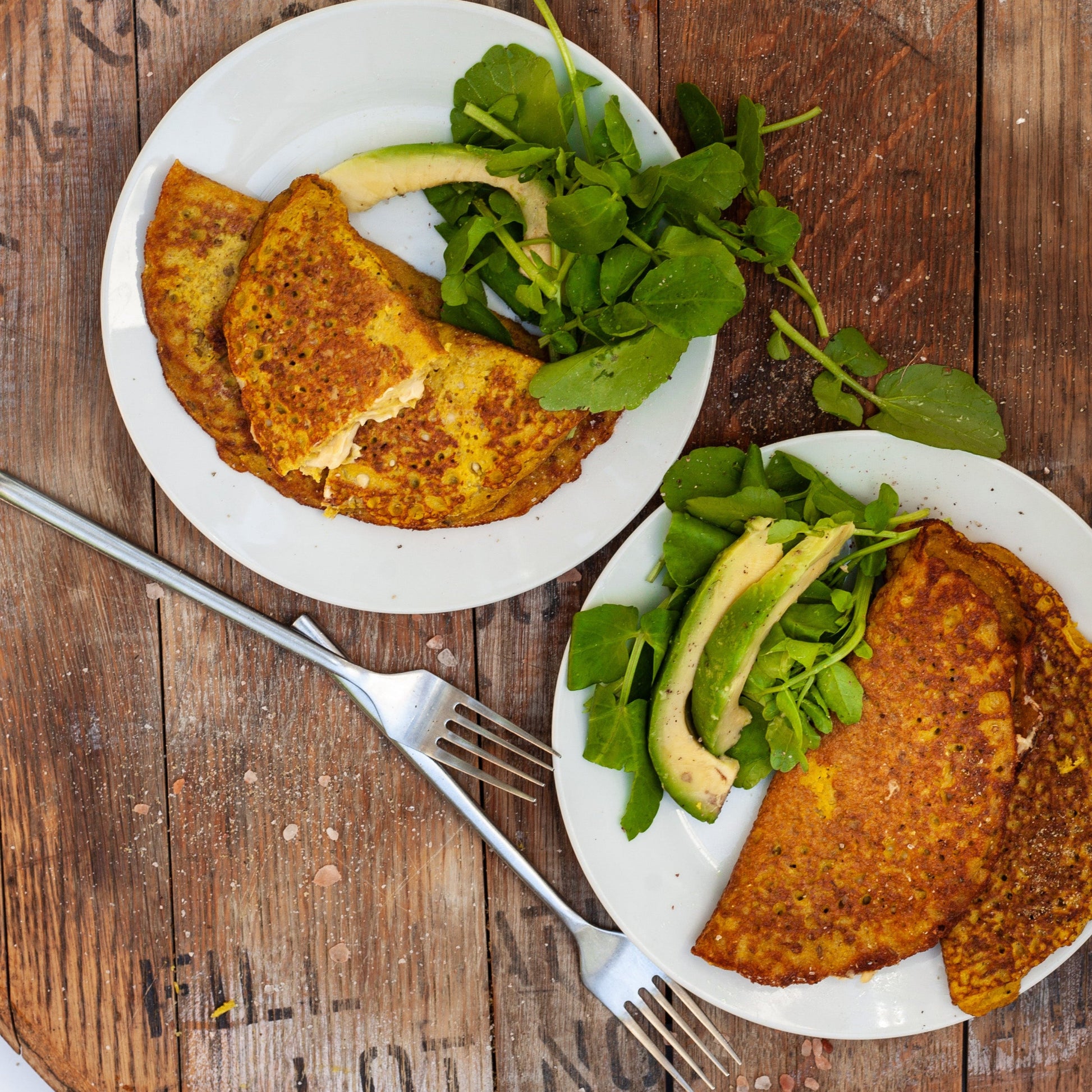 Two plates of vegan mung bean omelette with avocado and greens on a wooden table