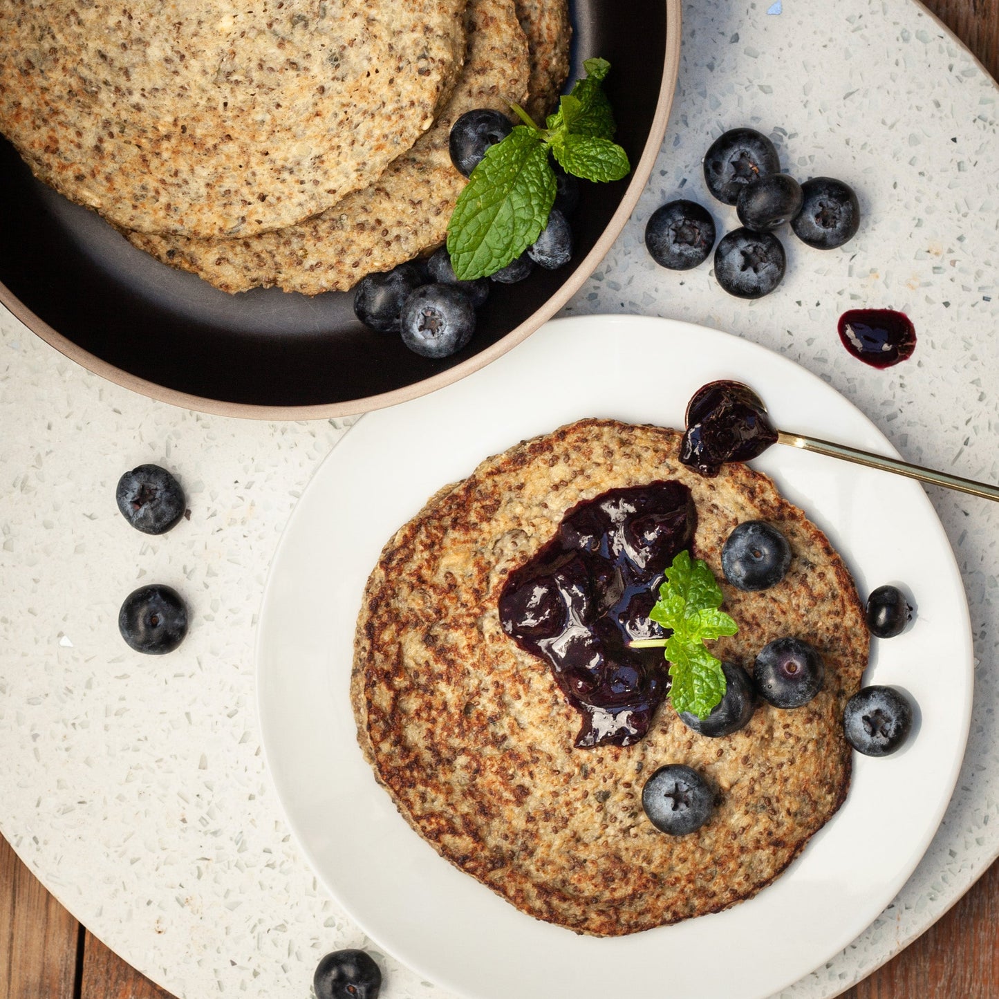 Two plates of vegan protein flapjacks served with blueberry puree on a wooden surface.