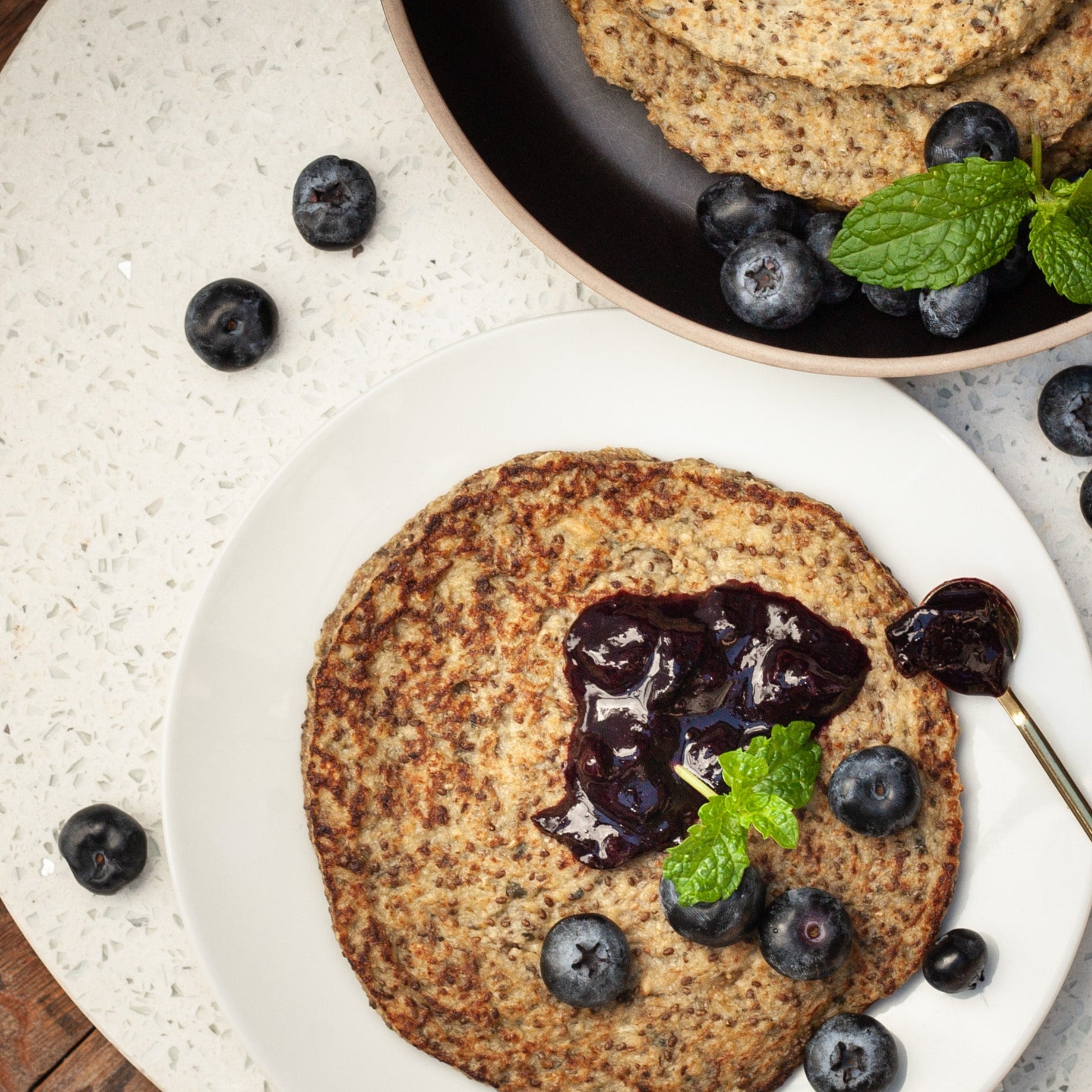Vegan protein flapjacks served with blueberry puree and fresh blueberries on a white plate.